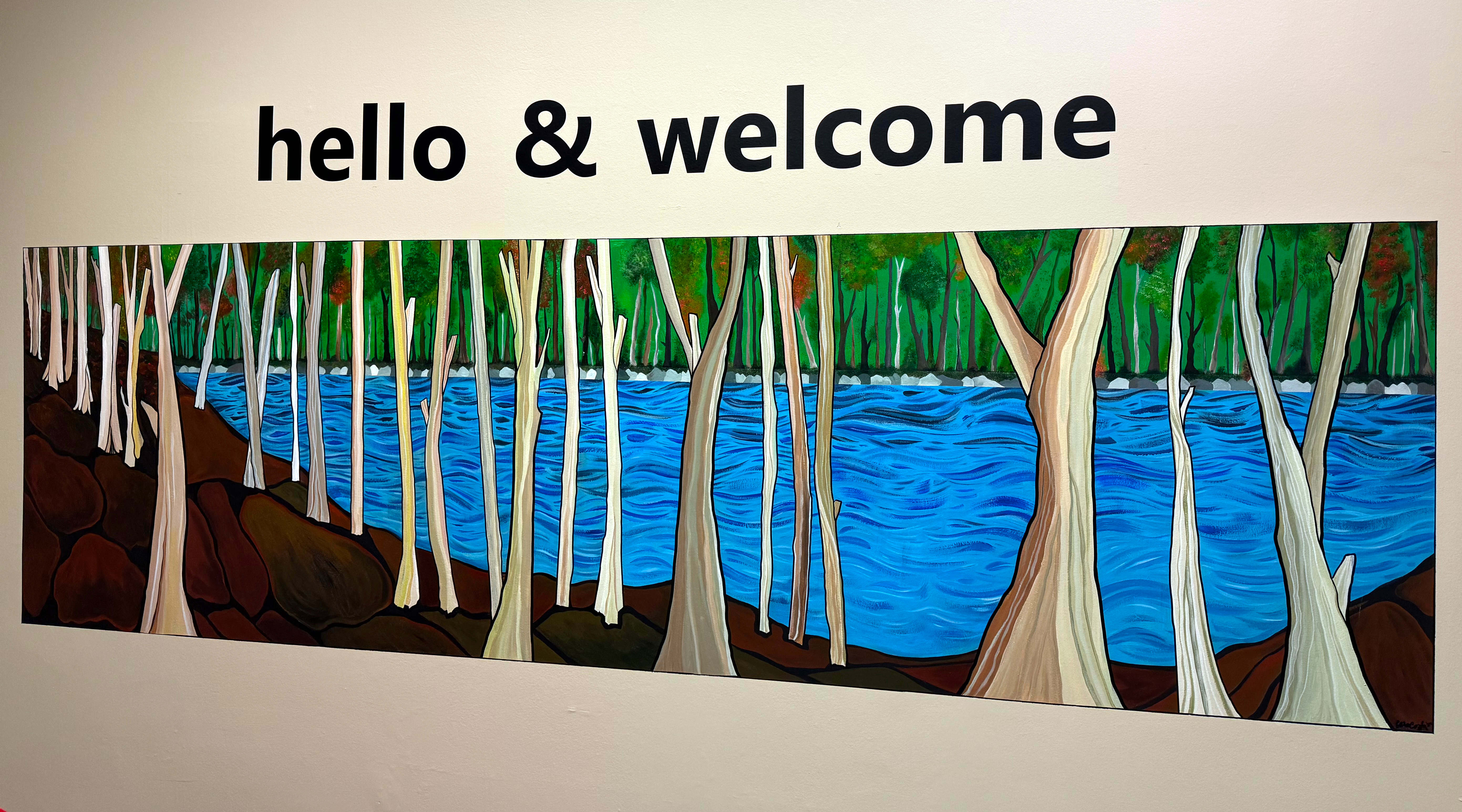 Hand painted mural of trees and a river with the words: Hello and Welcome above it.