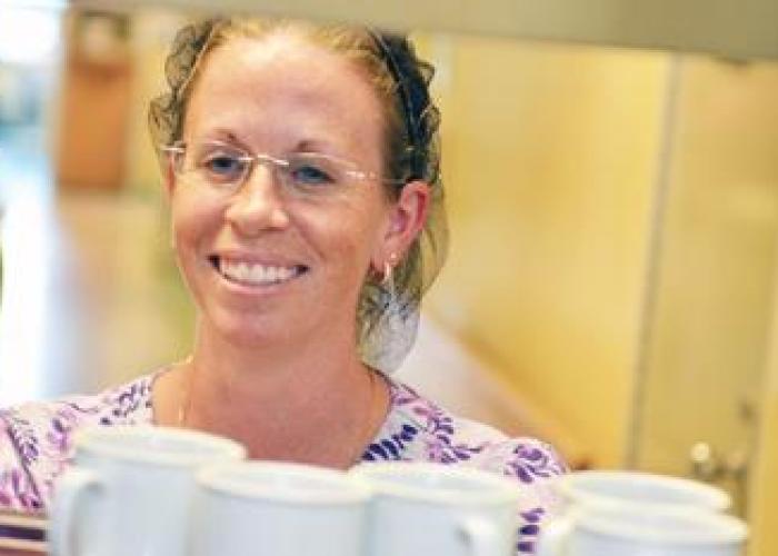 A member of Food Services moves a tray of mugs